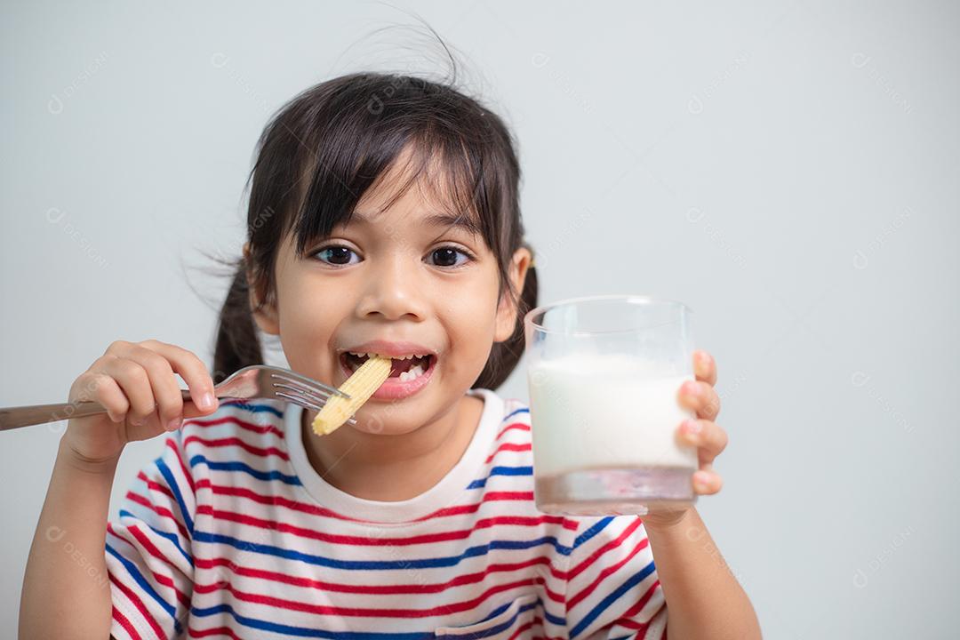 Linda garota asiática comendo vegetais saudáveis ​​e leite para ela