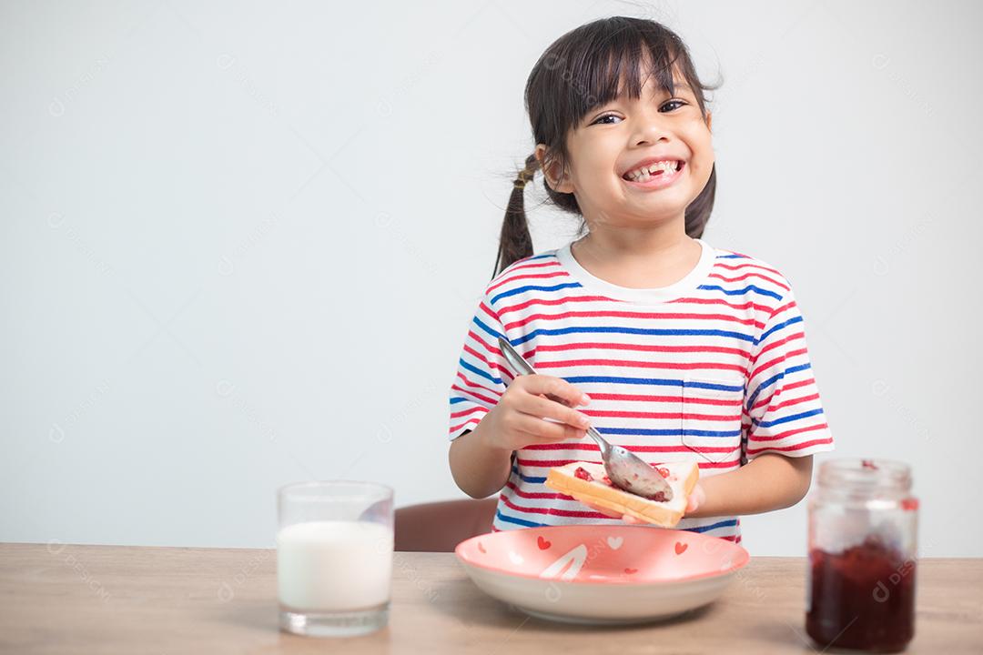 Menina asiática tomando café da manhã com pão e geleia com um copo de leite