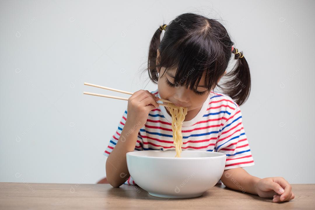Linda garota asiática comendo deliciosos macarrão instantâneo em casa.