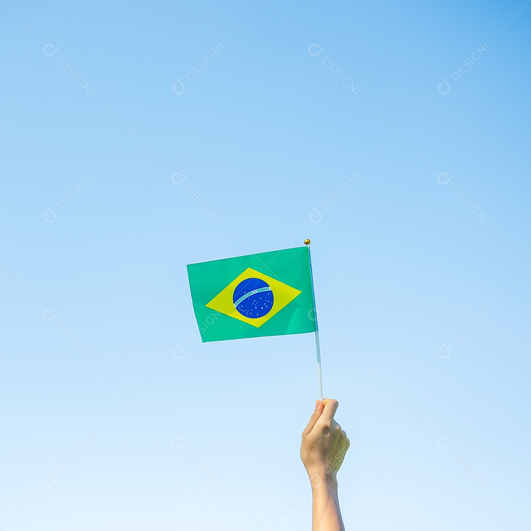 mão segurando a bandeira do Brasil sobre fundo de céu azul. Dia da independência de setembro e conceitos de celebração feliz