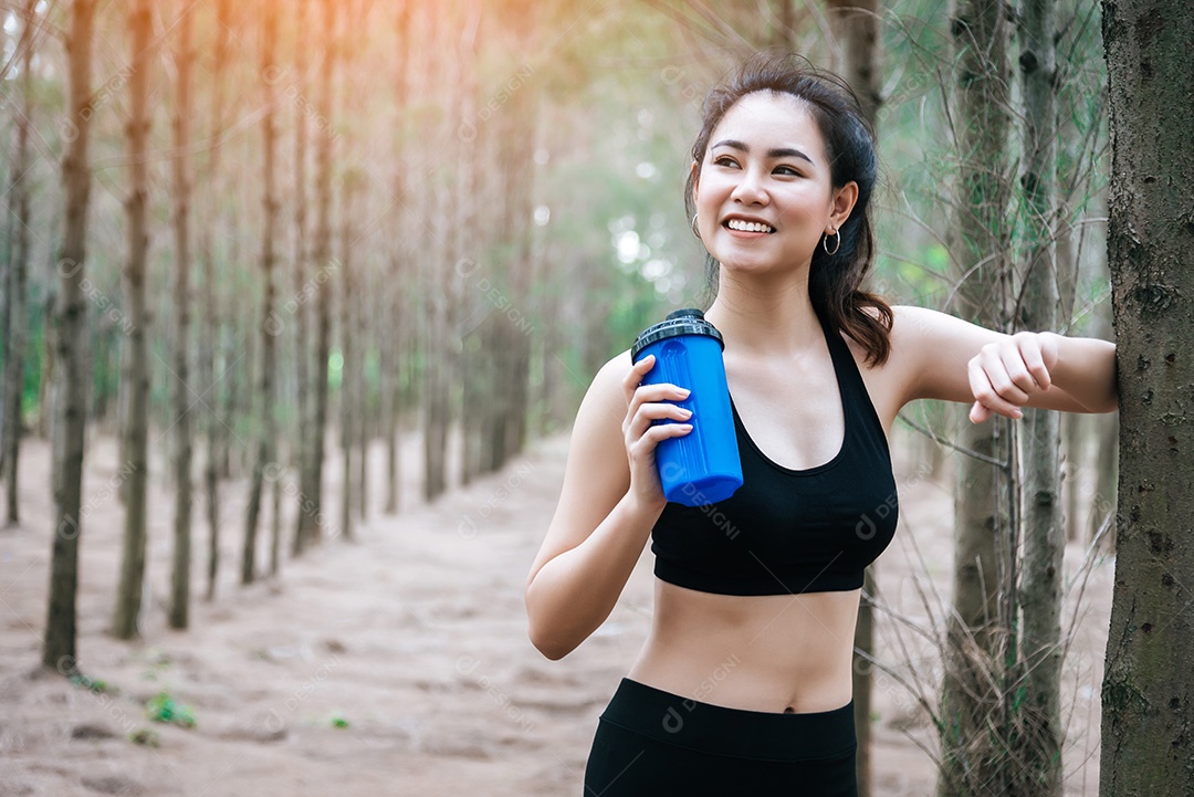 Água potável de mulher de beleza asiática na floresta. Esporte e Saudável.