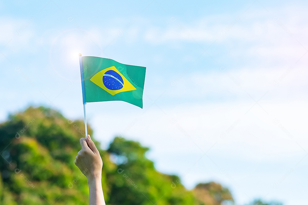 mão segurando a bandeira do Brasil sobre fundo de céu azul. Dia da independência de setembro e conceitos de celebração feliz