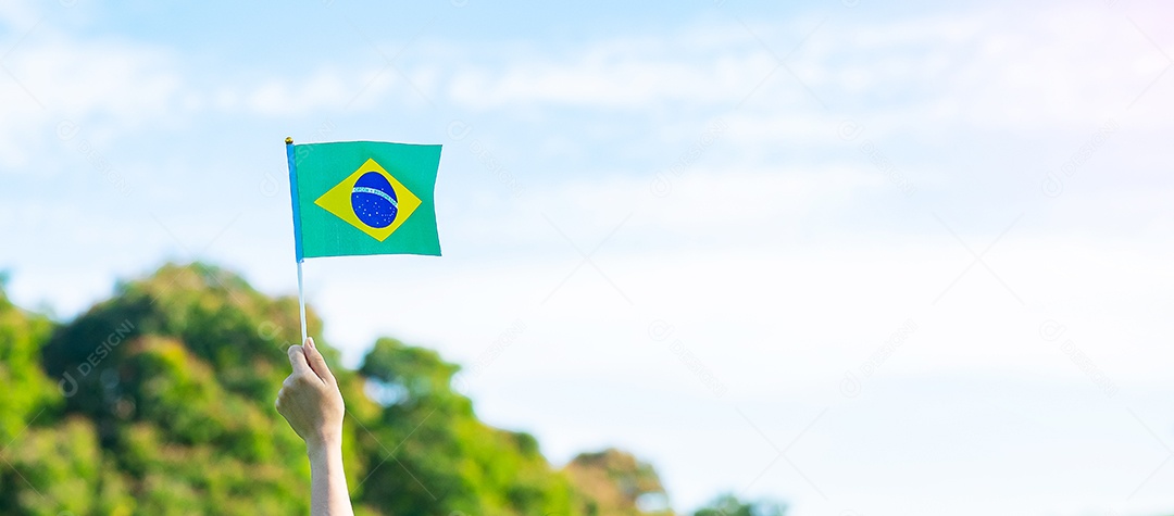 mão segurando a bandeira do Brasil sobre fundo de céu azul. Dia da independência de setembro e conceitos de celebração feliz