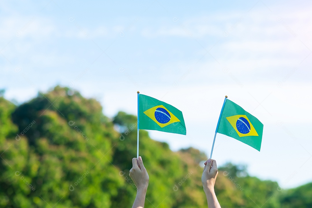 mão segurando a bandeira do Brasil sobre fundo de céu azul. Dia da independência de setembro e conceitos de celebração feliz
