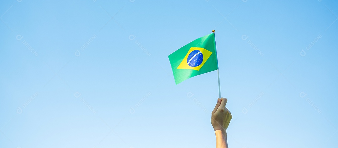 mão segurando a bandeira do Brasil sobre fundo de céu azul. Dia da independência de setembro e conceitos de celebração feliz