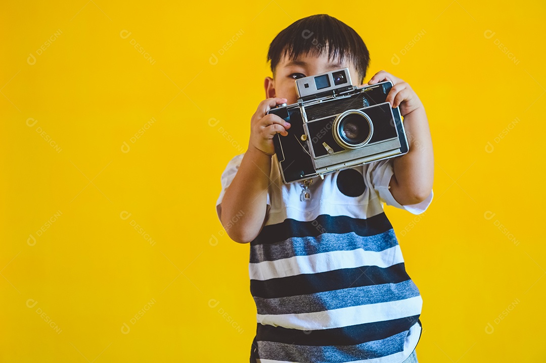 Rapaz asiático segurando a velha câmera vintage e posando como fotografia em fundo amarelo isolado. Estilo de vida de pessoas e conceito de tecnologia.