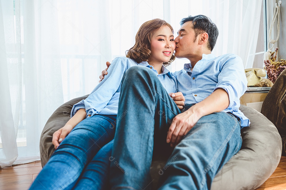 Casal asiático se beijando no sofá na sala de casa doméstica no dia dos namorados. Estilo de vida e conceito de família de felicidade.