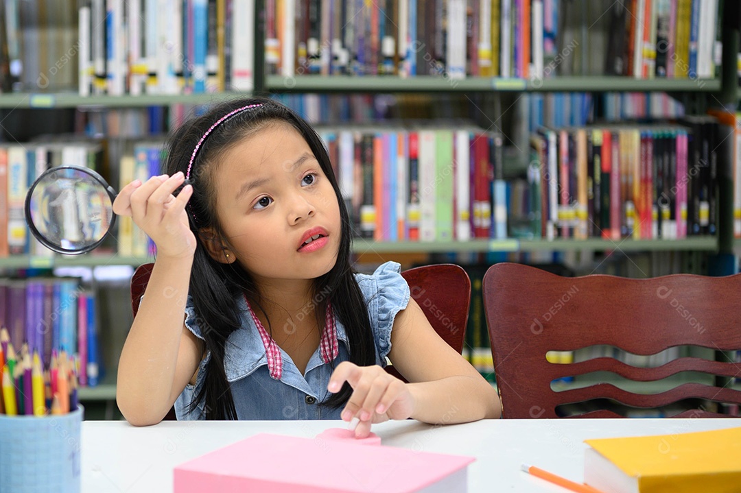Menina asiática segurando lupa e pensando na biblioteca da escola. Conceito de educação e aprendizagem.