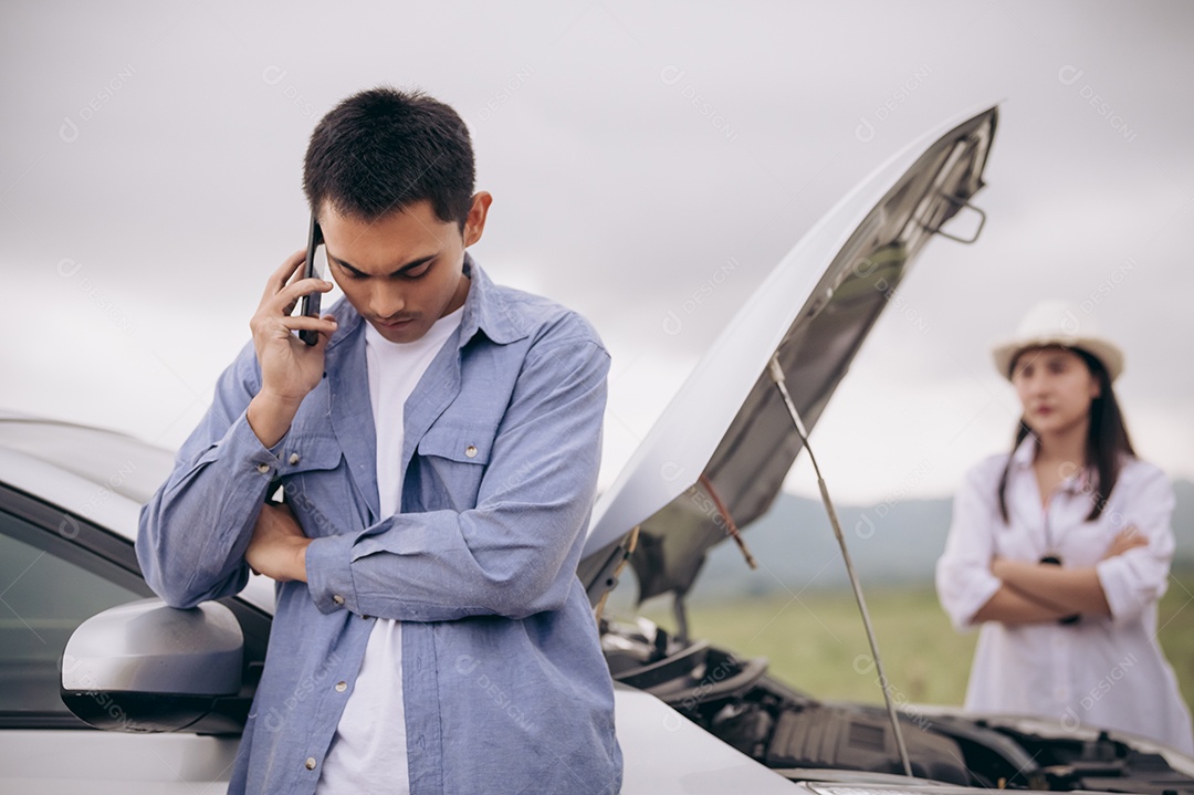 Homem asiático ligando para o serviço de manutenção de carros com a namorada olhando para ele entre uma longa viagem.