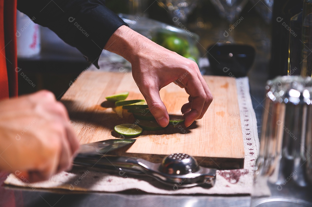 Close-up da mão de barman profissional cortando limão para fazer suco de limonada por faca em boate.