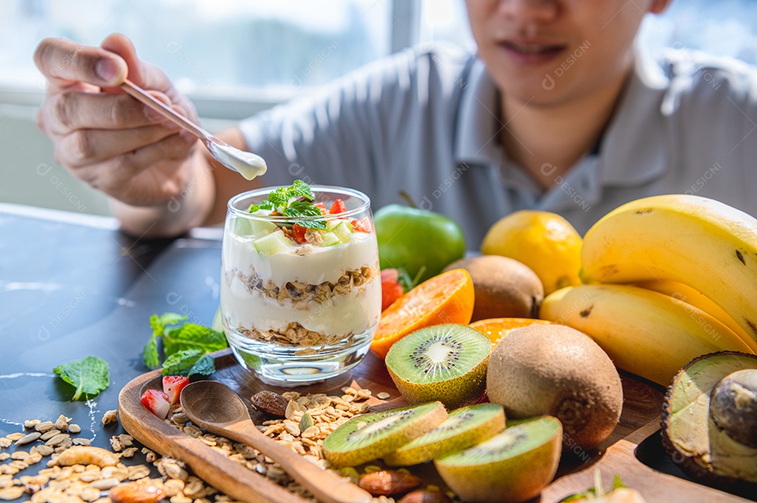 Close-up de muitos iogurte de frutas com granola e homem pegando a mão na mesa no fundo da cozinha. Conceito de ingrediente de alimentos e bebidas.