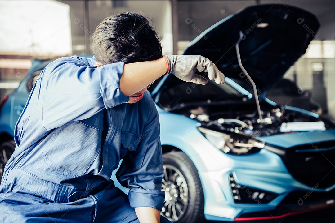 Mecânico de automóveis descansando de exaustão e enxugando o suor do trabalho árduo e cansado na garagem da oficina mecânica.