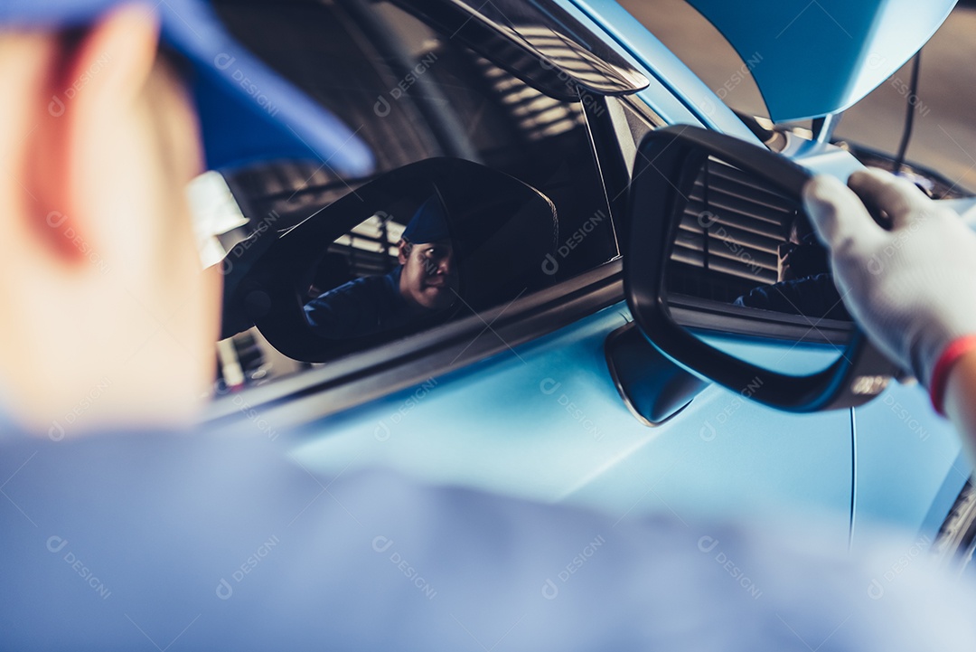 O técnico do carro mecânico está olhando para o espelho retrovisor para verificar o veículo de manutenção pelo pedido de reclamação do cliente na garagem da oficina mecânica.