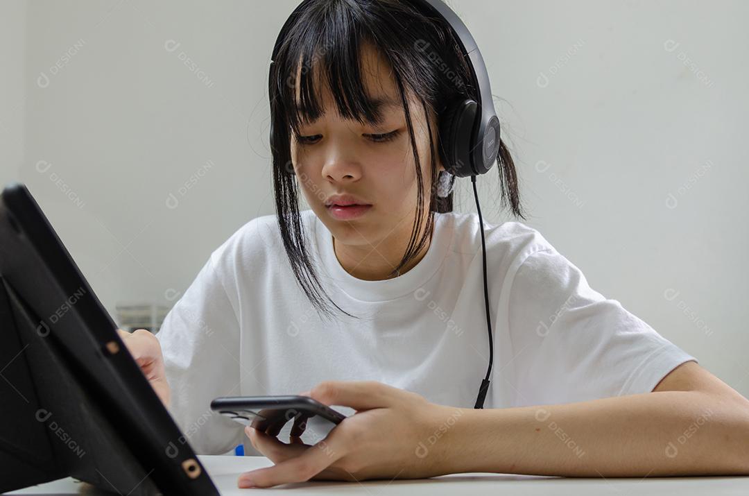 Menina segurando caneta escrevendo livro estudo aprendendo digital internet vídeo computador on-line laptop em casa.