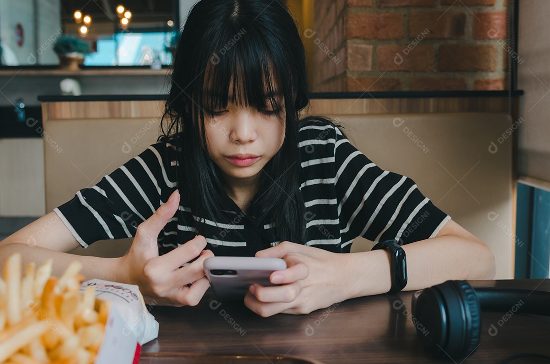 Adolescente usando fones de ouvido e segurando uma mídia social de smartphone celular relaxando no sofá.