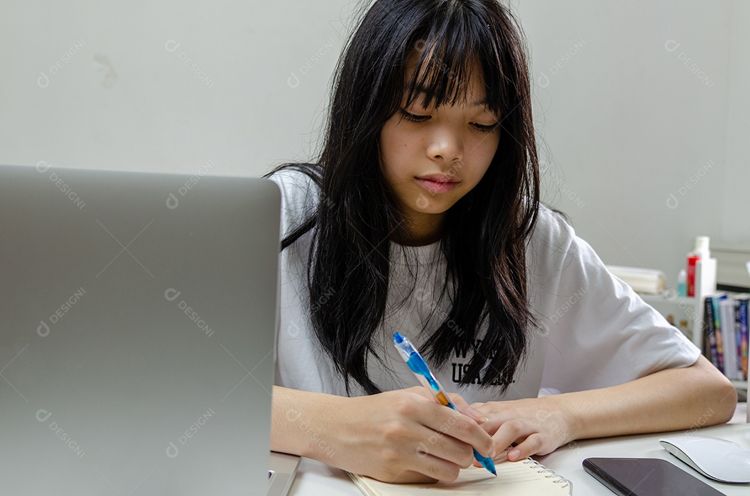 menina segurando caneta escrevendo livro estudo aprendendo digital internet vídeo computador on-line laptop em casa.