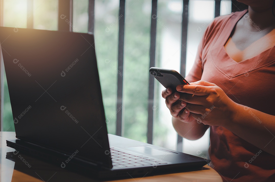 Mão de uma mulher segurando a tecnologia on-line de marketing digital de smartphone móvel e rede social de comunicação com computador portátil navegação na internet e compras on-line no conceito de mesa.