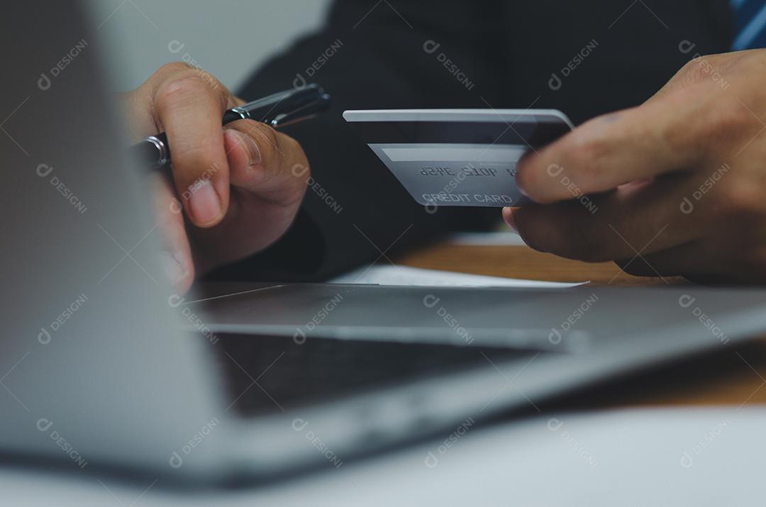 Mão de homem segurando cartão de crédito usando tecnologia de Internet digital para pagar suas compras e compras on-line em um computador.