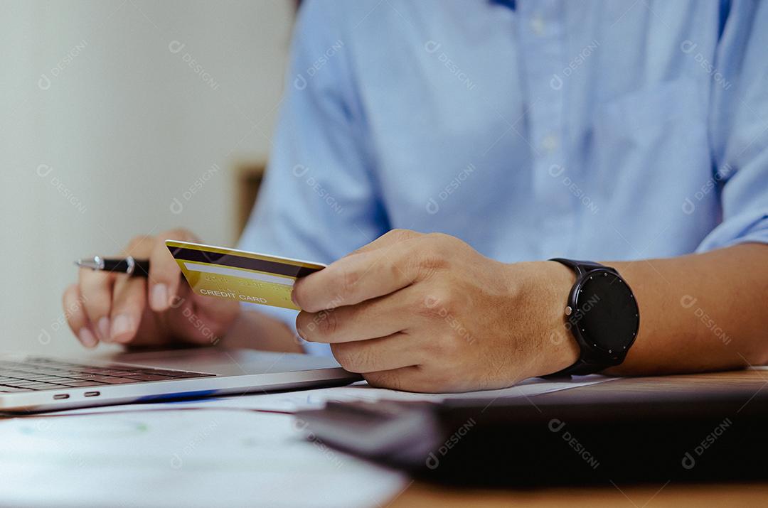 Mão de homem segurando cartão de crédito usando tecnologia de Internet digital para pagar suas compras e compras on-line em um computador.