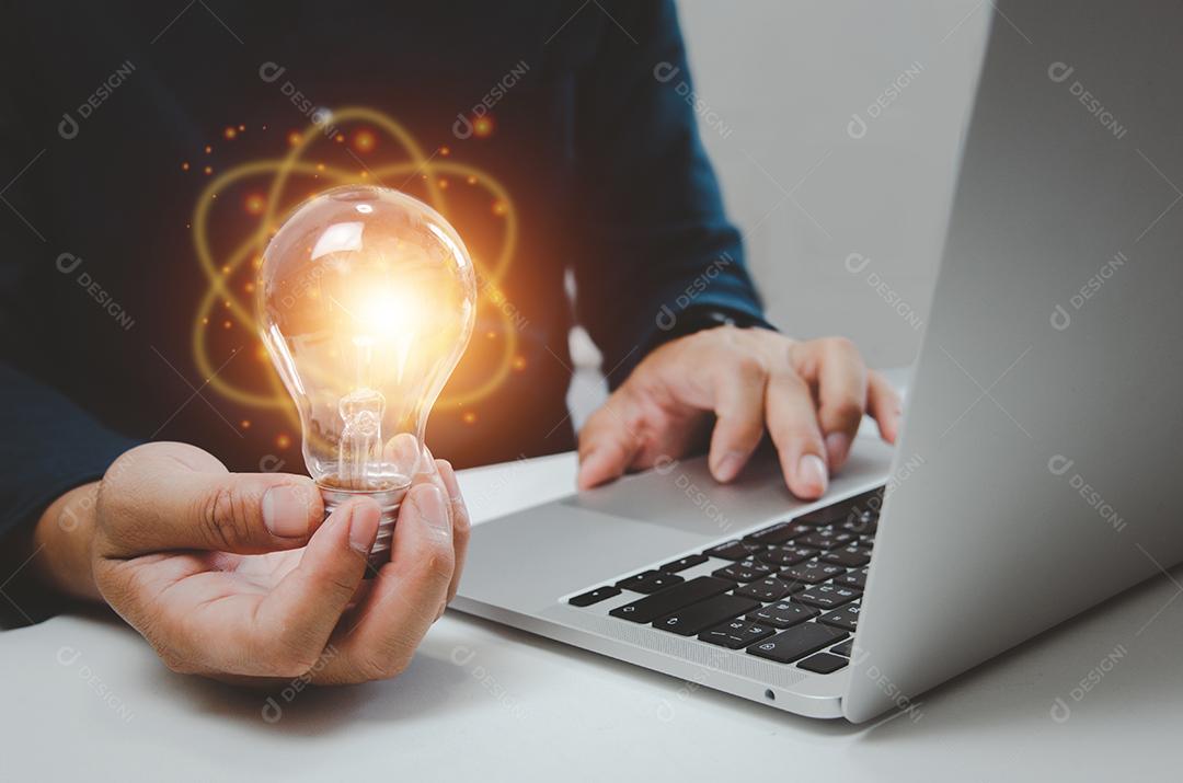 Homem de mão segurando a inspiração de criatividade de ideia de lâmpada e usando o computador portátil na mesa.