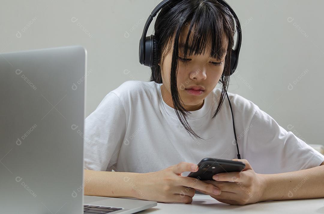 Garota usando fones de ouvido estudando on-line com o laptop do computador e ouvindo música relaxante ou reproduzindo mídias sociais da internet em casa.