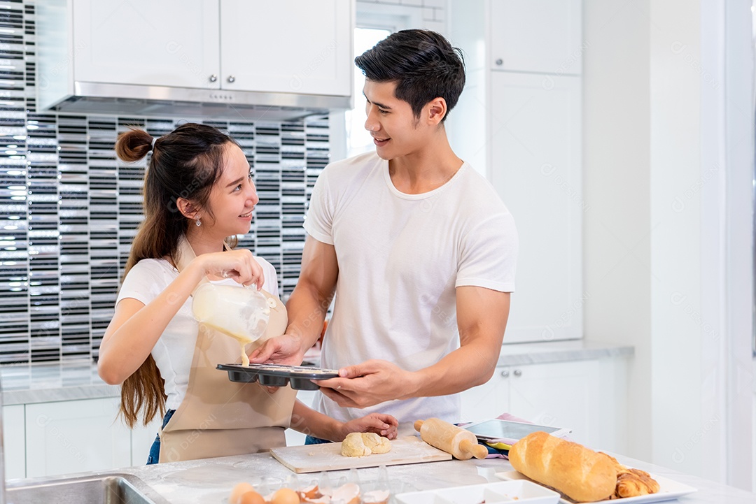 Casais asiáticos felizes cozinhando e assando bolo juntos na cozinha. Homem e mulher que procuram tablet seguem a etapa da receita em casa. Conceito de amor e felicidade. Doce lua de mel e tema do dia dos namorados.