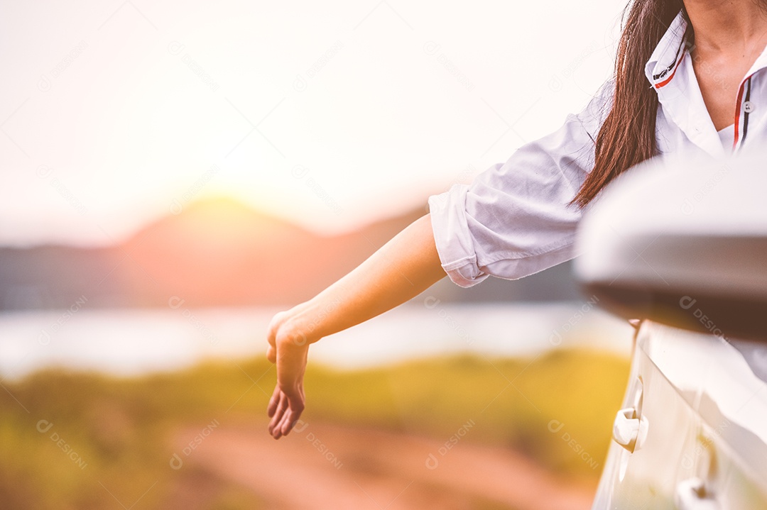 Mulher feliz acenando com a mão do lado de fora do carro de janela aberta com prado e fundo de lago de montanha.