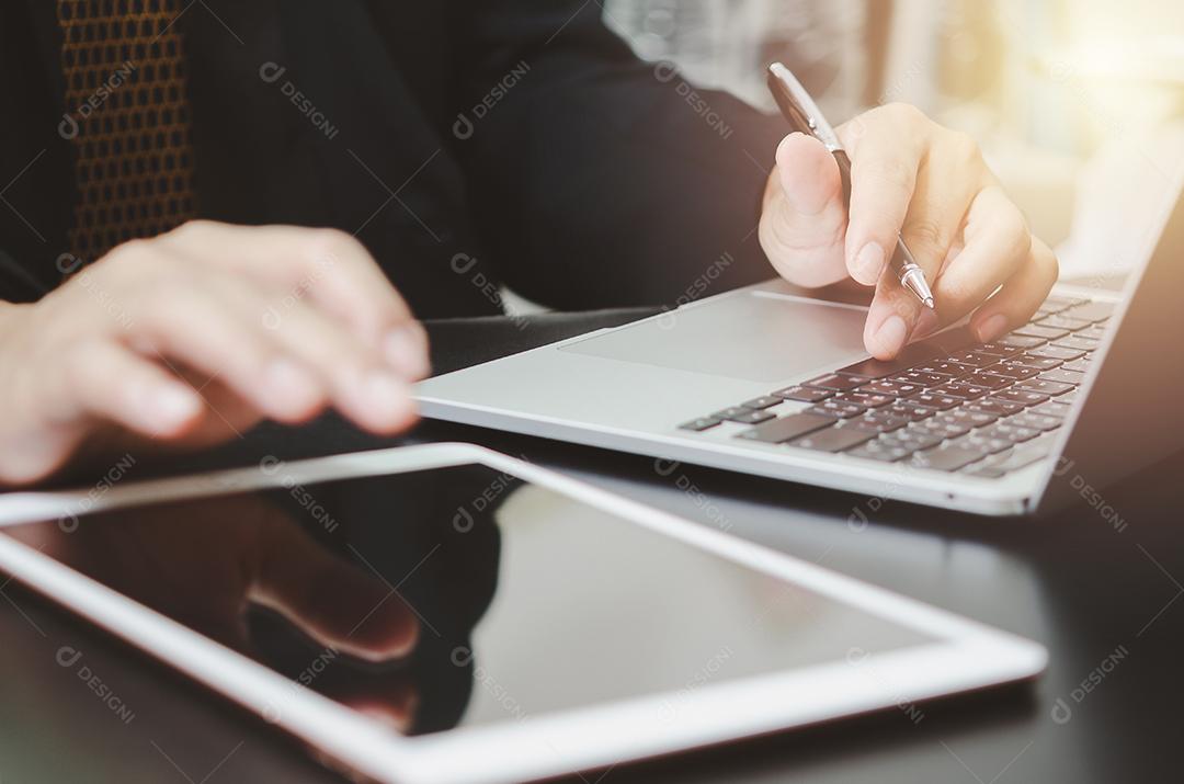 Empresário segurando a caneta digitando teclado computador laptop e tablet na mesa. Conceito de pesquisa e comunicação de trabalho de internet digital de tecnologia de negócios.