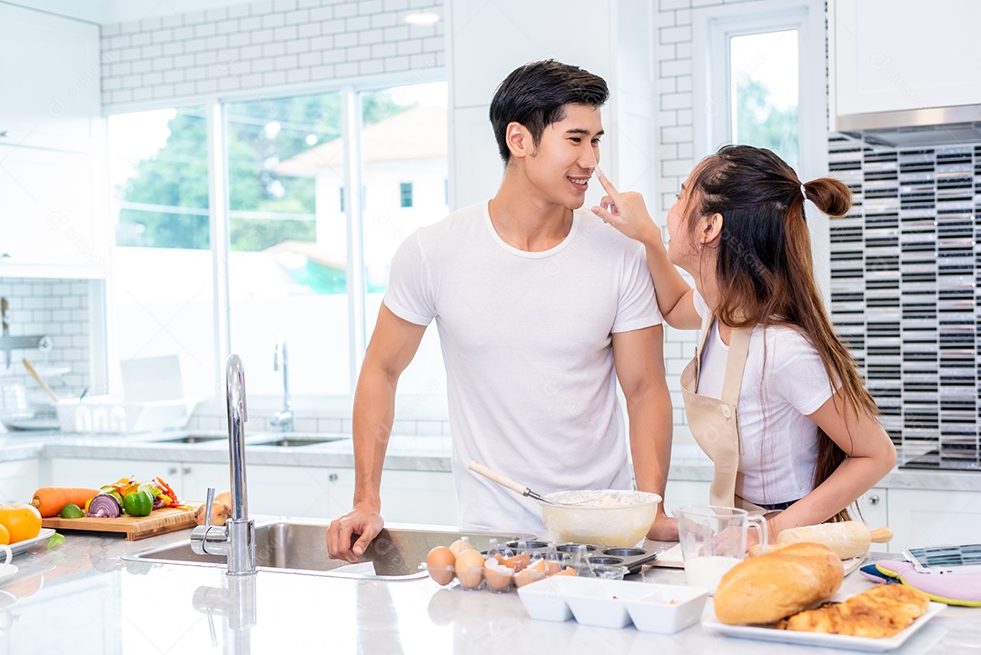 Casais asiáticos felizes cozinhando e assando bolo juntos na cozinha. Homem e mulher que procuram tablet seguem a etapa da receita em casa. Conceito de amor e felicidade. Doce lua de mel e tema do dia dos namorados.