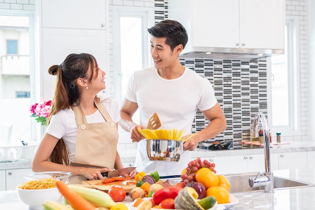 Casal jovem asiático feliz se prepara para fazer espaguete à bolonhesa na cozinha. Namorado e namorada cozinhando juntos. Estilo de vida de pessoas e conceito de relacionamento romântico.
