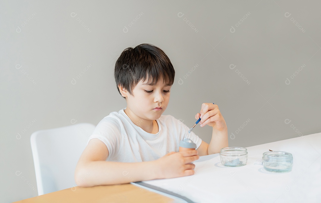 Garoto da escola de retrato usando pincéis pintando cor cinza no ovo e trabalhos de casa de decorações de Páscoa DIY