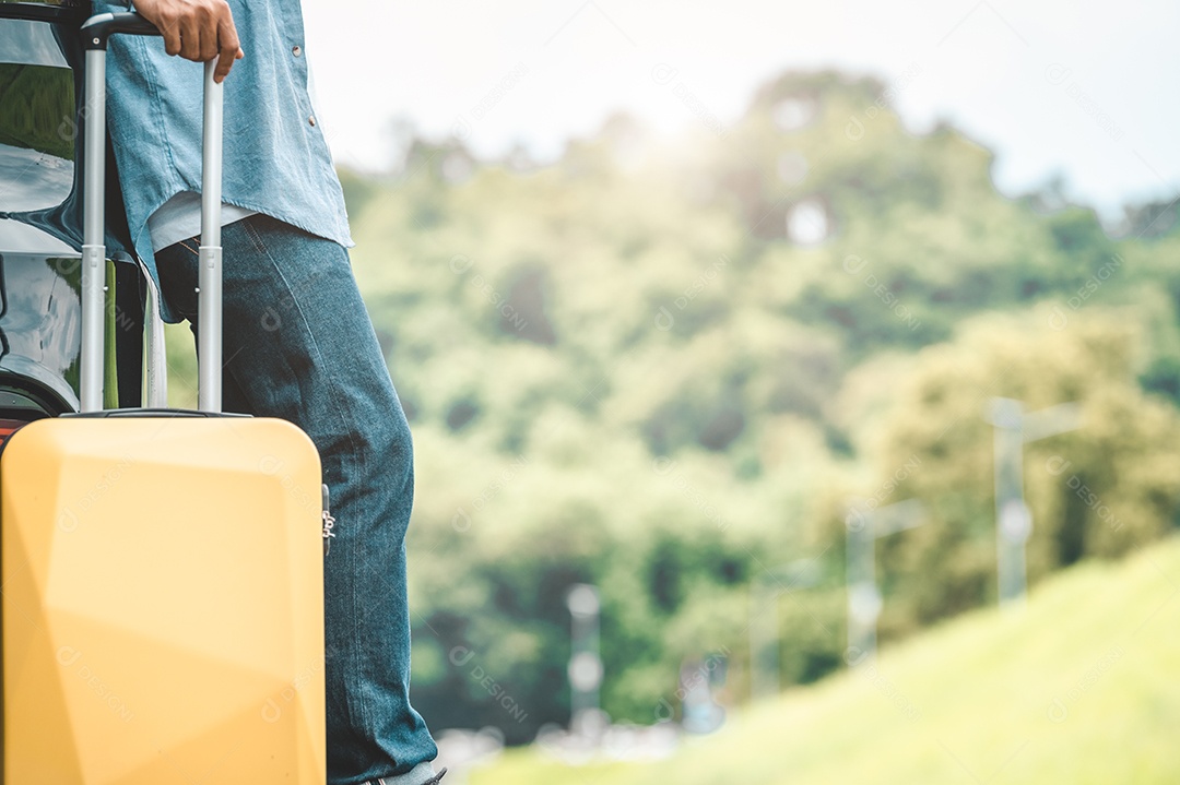 Close-up of man's legs resting during travel on trip with yellow suitcase on summer nature background.