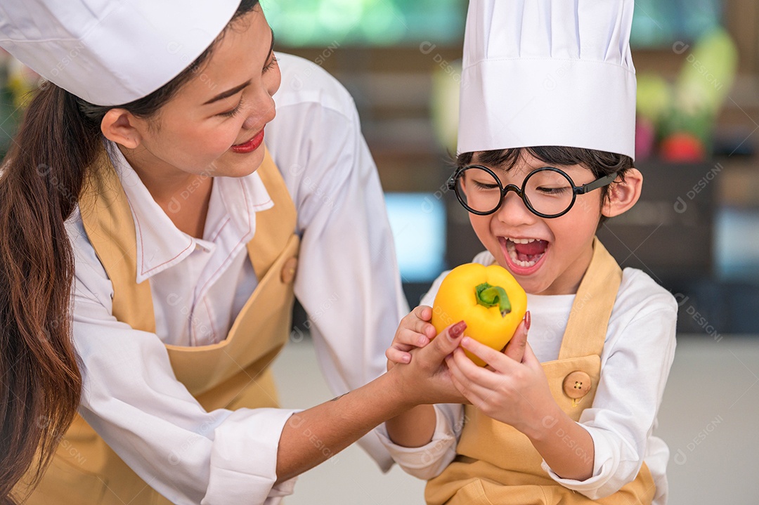 Retrato bonito pequeno chef de menino feliz asiático interessado em cozinhar com a mãe engraçada na cozinha de casa.