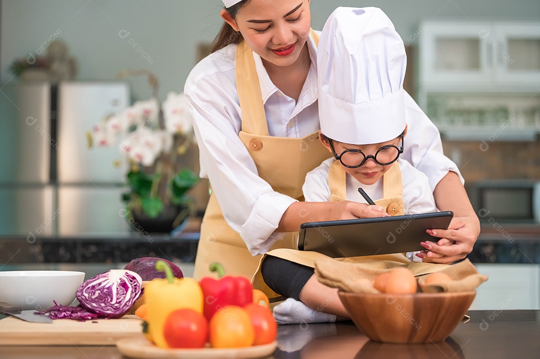 Mãe de beleza asiática e menino bonitinho preparam compras on-line e listam ingredientes para cozinhar na cozinha em casa com tablet.