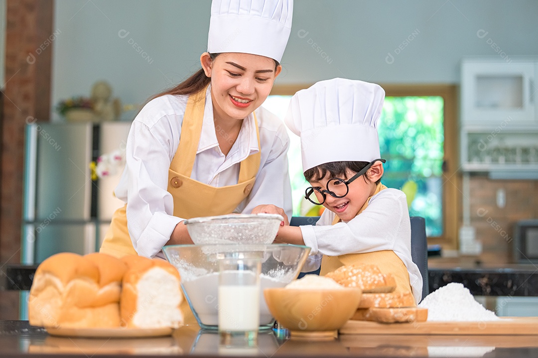Menino asiático bonitinho e linda mãe peneirando farinha de massa com peneira peneira na cozinha de casa na mesa para se preparar para assar padaria e bolo.