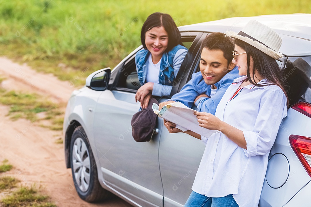 Mulher asiática feliz e seus amigos de pé de carro na estrada costeira ao pôr do sol. Jovem se divertindo durante a viagem.
