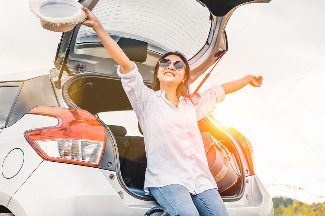 Mulher asiática feliz abre os braços sob o pôr do sol à beira-mar com fundo de natureza durante viagens de férias.