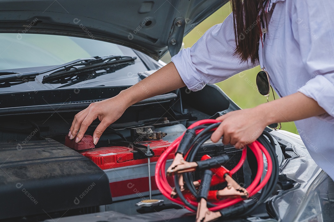 Close-up da mão de uma mulher segurando o fio de cobre do cabo da bateria para reparar o carro quebrado conectando a bateria com a linha vermelha e preta ao terminal elétrico sozinha.