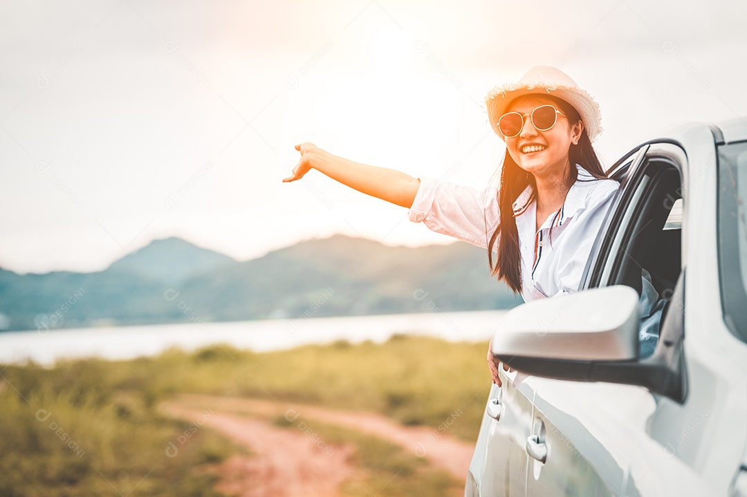 Mulher feliz acenando com a mão do lado de fora do carro de janela aberta com prado e fundo de lago de montanha.