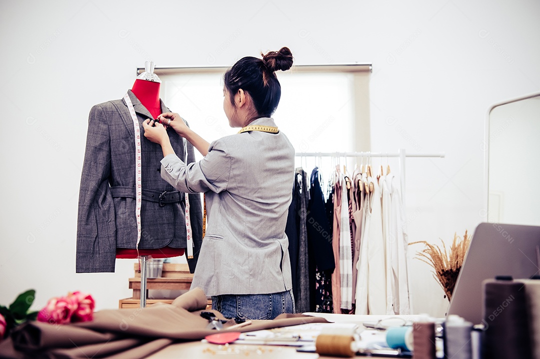 Menina estilista asiática fazendo ajuste no terno formal.