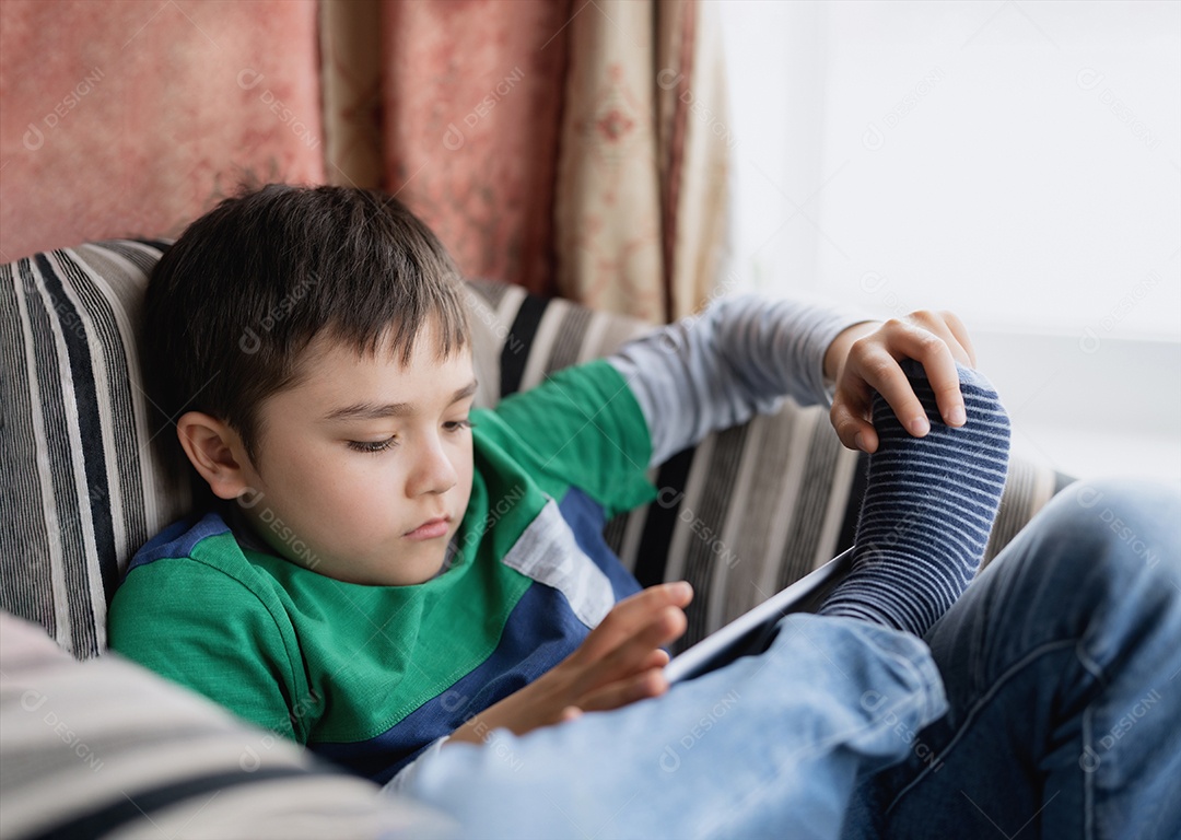 Garoto de retrato jogando jogo no tablet sentado no sofá, Menino lendo ou fazendo lição de casa online na internet em casa