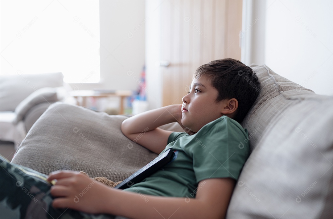 Garoto com controle remoto e olhando para cima com cara curiosa, Menino sentado no sofá assistindo desenho animado na TV