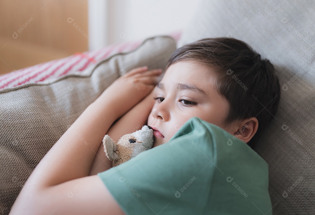 Garoto com controle remoto e olhando para cima com cara curiosa, Menino sentado no sofá assistindo desenho animado na TV