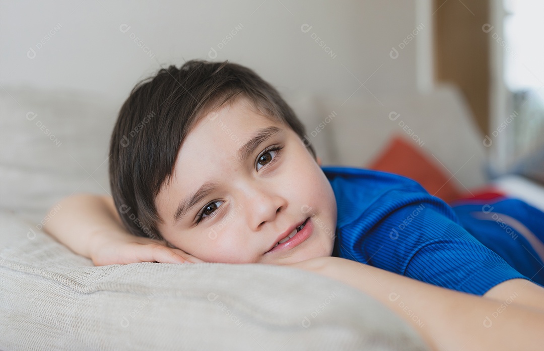 Garoto feliz deitado no sofá olhando para a câmera com um rosto sorridente