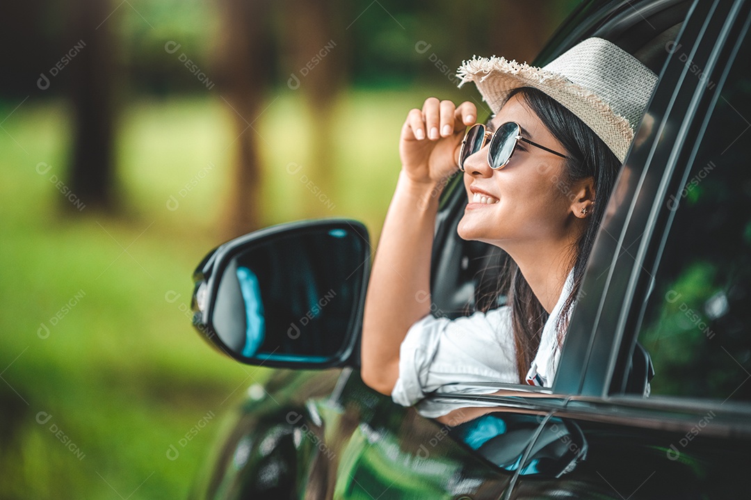 Mão de uma mulher feliz segurando o chapéu do lado de fora do carro de janela aberta com verde.