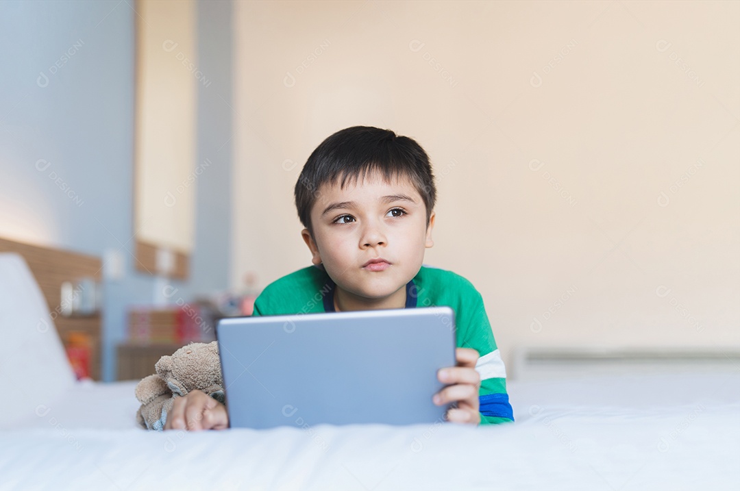 Garoto de retrato jogando jogos on-line na internet no quarto, Menino usando tablet digitando ou conversando com um amigo pela manhã