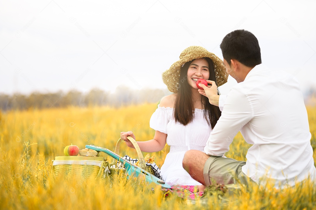 Casal asiático fazendo piquenique no campo de grama prado de outono dourado.