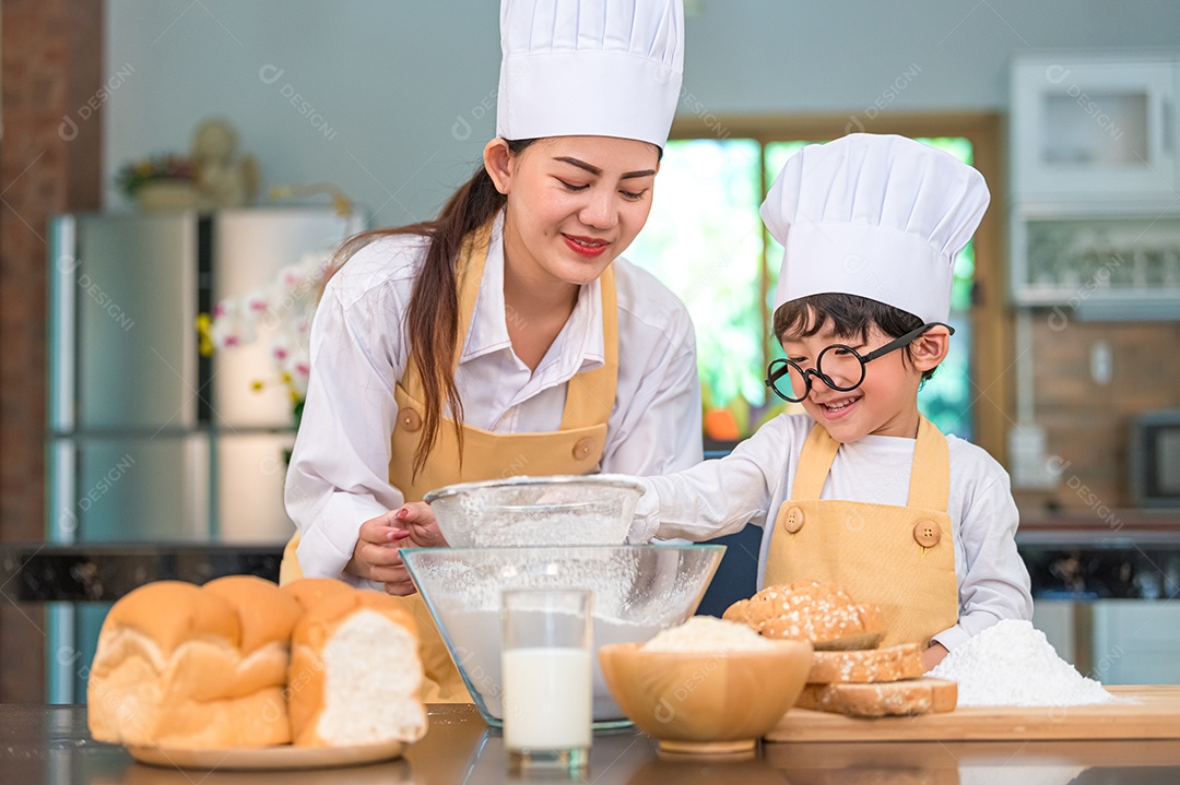 Menino asiático bonitinho e linda mãe peneirando farinha de massa.