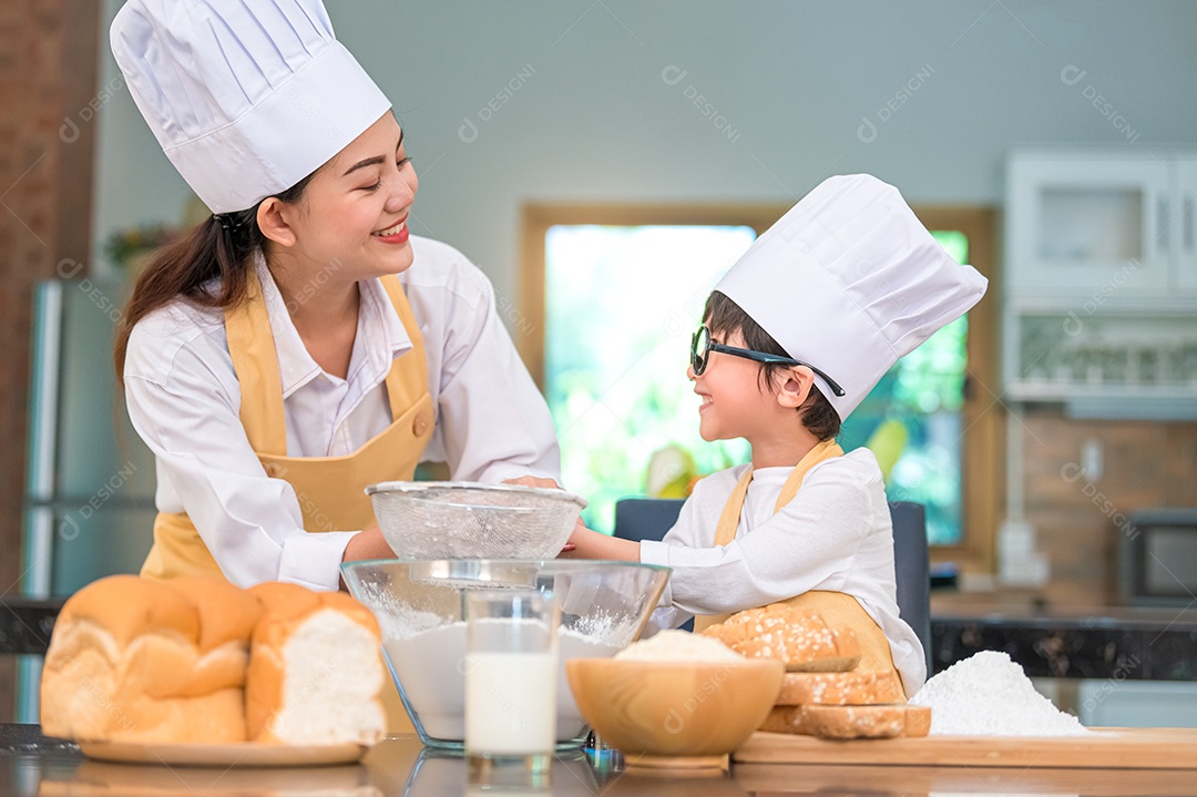 Menino asiático bonitinho e linda mãe peneirando farinha de massa.