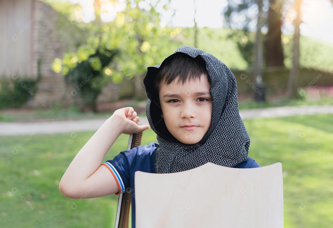 Menino vestindo fantasia de cavaleiro segurando escudo de espada em pé no parque